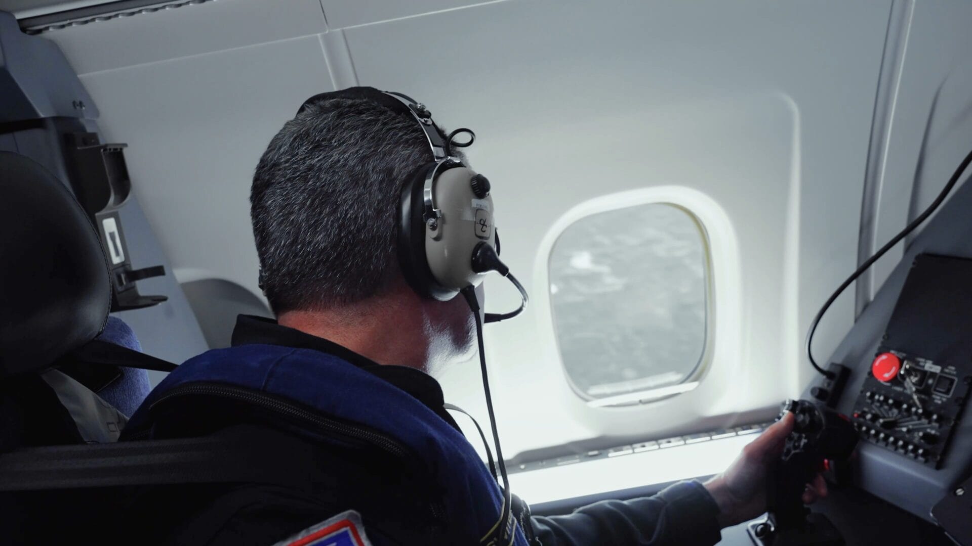 Sensor operator at workstation looking out window of aircraft over the ocean