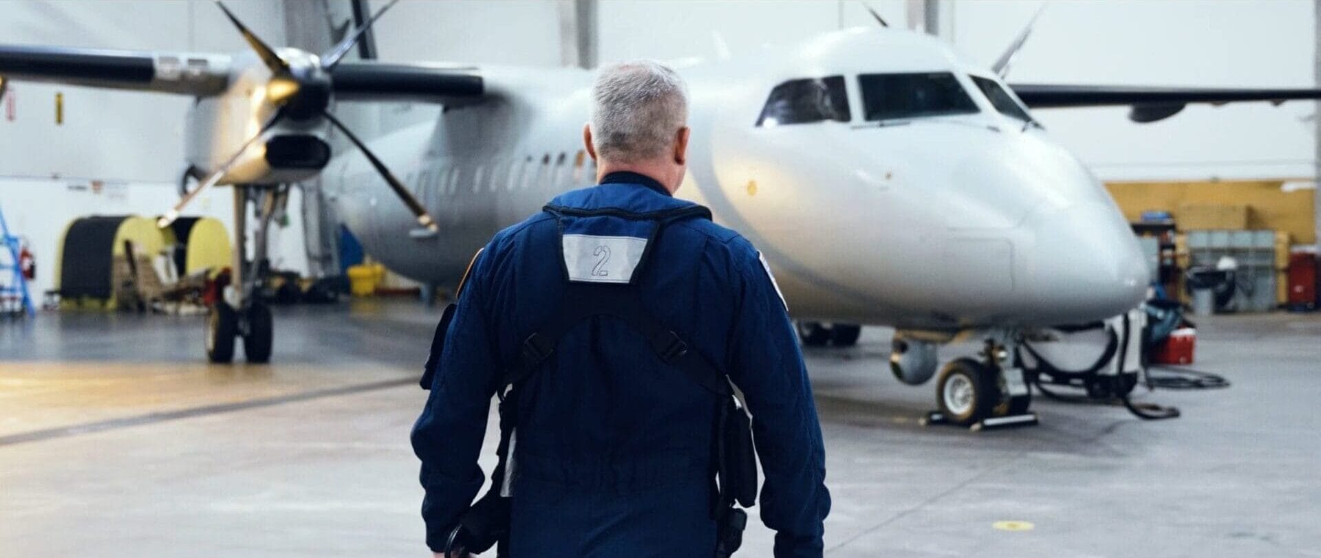 Pilot in flight suit back-on walking toward aircraft in a hangar
